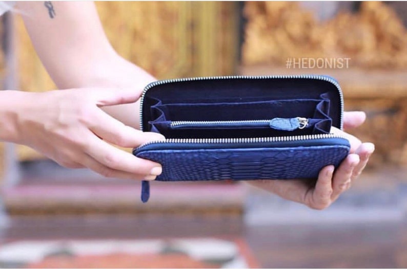 May include: A blue leather wallet with a zipper closure and a snakeskin pattern. The wallet is open and empty, showing the interior lining. The text #HEDONIST is visible in the top right corner of the image.