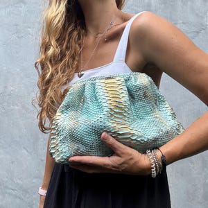 May include: A light blue and gold snakeskin clutch purse with a gathered design.