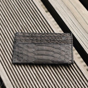 Puede incluir: Un tarjetero de cuero negro con un patr&oacute;n de piel de serpiente. El tarjetero est&aacute; sobre una superficie de madera.