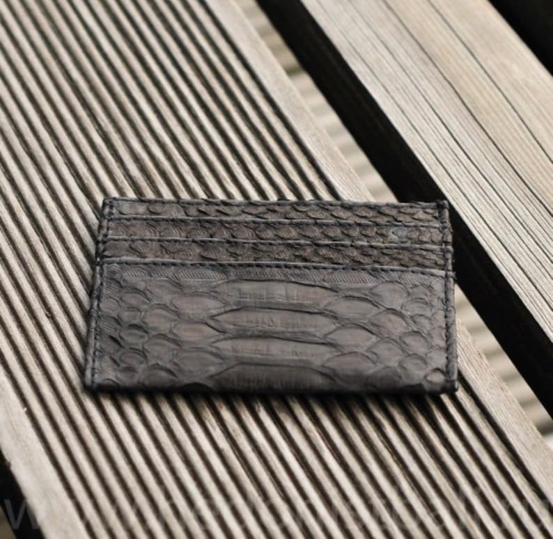 Puede incluir: Un tarjetero de cuero negro con un patr&oacute;n de piel de serpiente. El tarjetero est&aacute; sobre una superficie de madera.