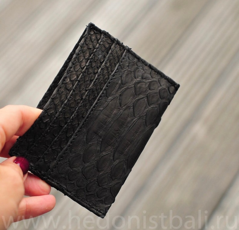 Puede incluir: Porta tarjetas de cuero negro con un patr&oacute;n texturizado y estampado. El porta tarjetas tiene m&uacute;ltiples ranuras para tarjetas.