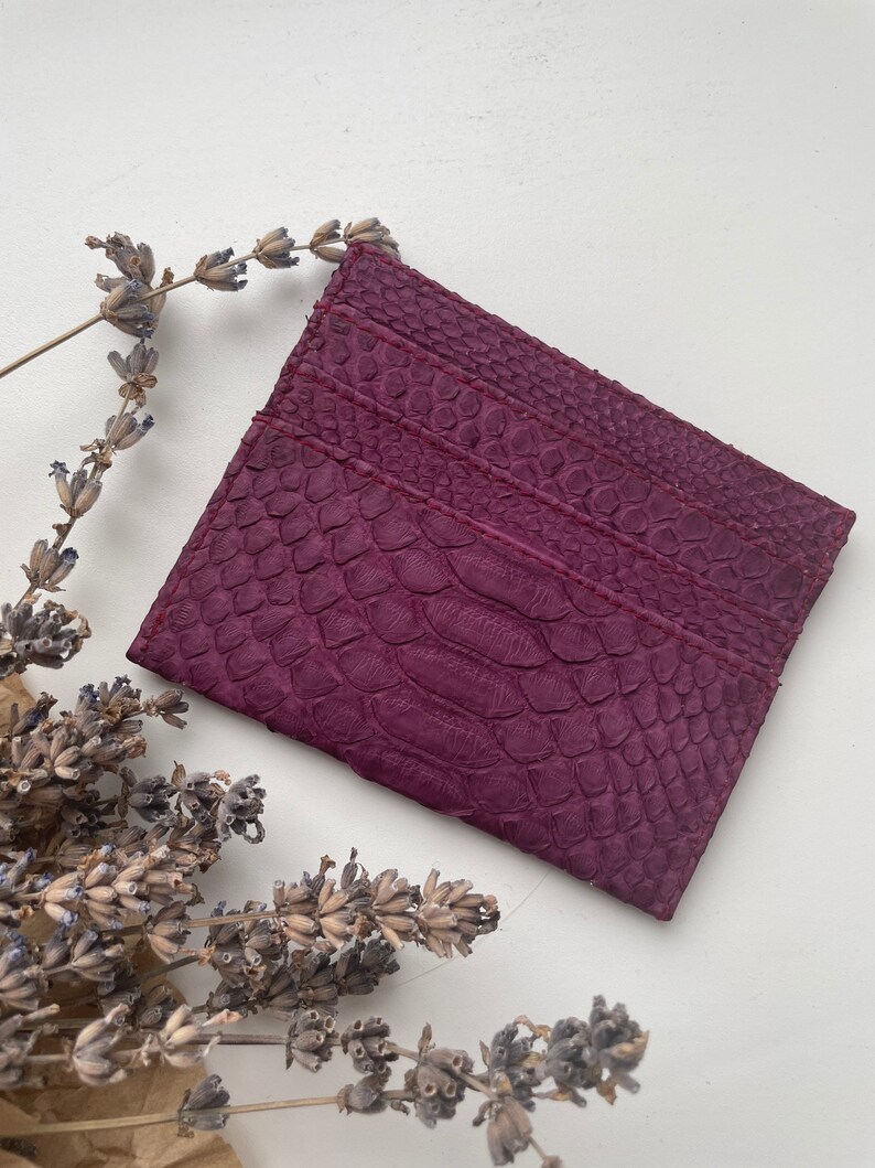 K&ouml;nnte beinhalten: Ein Kartenetui aus violettem Leder mit einem strukturierten Muster, das an Schlangenhaut erinnert.