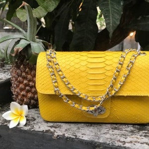 May include: A bright yellow leather handbag with a chain strap. The bag has a snakeskin pattern and a silver clasp.