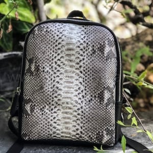 Könnte beinhalten: Ein schwarzer Lederrucksack mit Schlangenhautmuster. Der Rucksack hat einen Reißverschluss und verstellbare Träger.