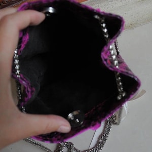 Op de afbeelding: Een klein roze en zwart handtasje met een zilveren kettingband. De tas is open en de binnenkant is zwart.