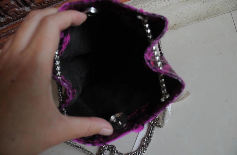Op de afbeelding: Een klein roze en zwart handtasje met een zilveren kettingband. De tas is open en de binnenkant is zwart.