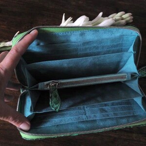 以下が含まれることがあります： ジッパー留めの緑色の革財布。財布が開いており、複数のカードスロットとジッパー付きのコンパートメントが見えます。