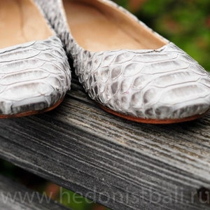 May include: Close-up of a pair of gray and white flats with a snakeskin pattern. The shoes have a rounded toe and a low heel. The shoes are made of a textured material and appear to be leather.