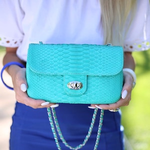 Könnte beinhalten: Eine türkisblaue Schlangenledertasche mit einer silbernen Kettenkette und einem silbernen Verschluss.