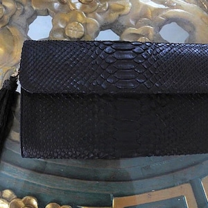 May include: A black snakeskin clutch bag with a black tassel.