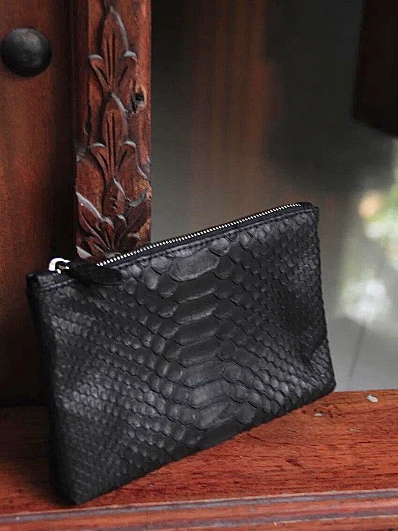 Może przedstawiać: Czarna kopert&oacute;wka ze sk&oacute;ry węża z srebrnym zamkiem błyskawicznym.