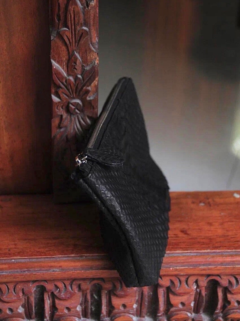 Może przedstawiać: Czarna sk&oacute;rzana kopert&oacute;wka z zamkiem błyskawicznym i wzorem sk&oacute;ry węża.