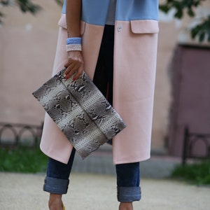 May include: A woman wearing a blue and pink long vest with a snakeskin clutch and yellow heels.