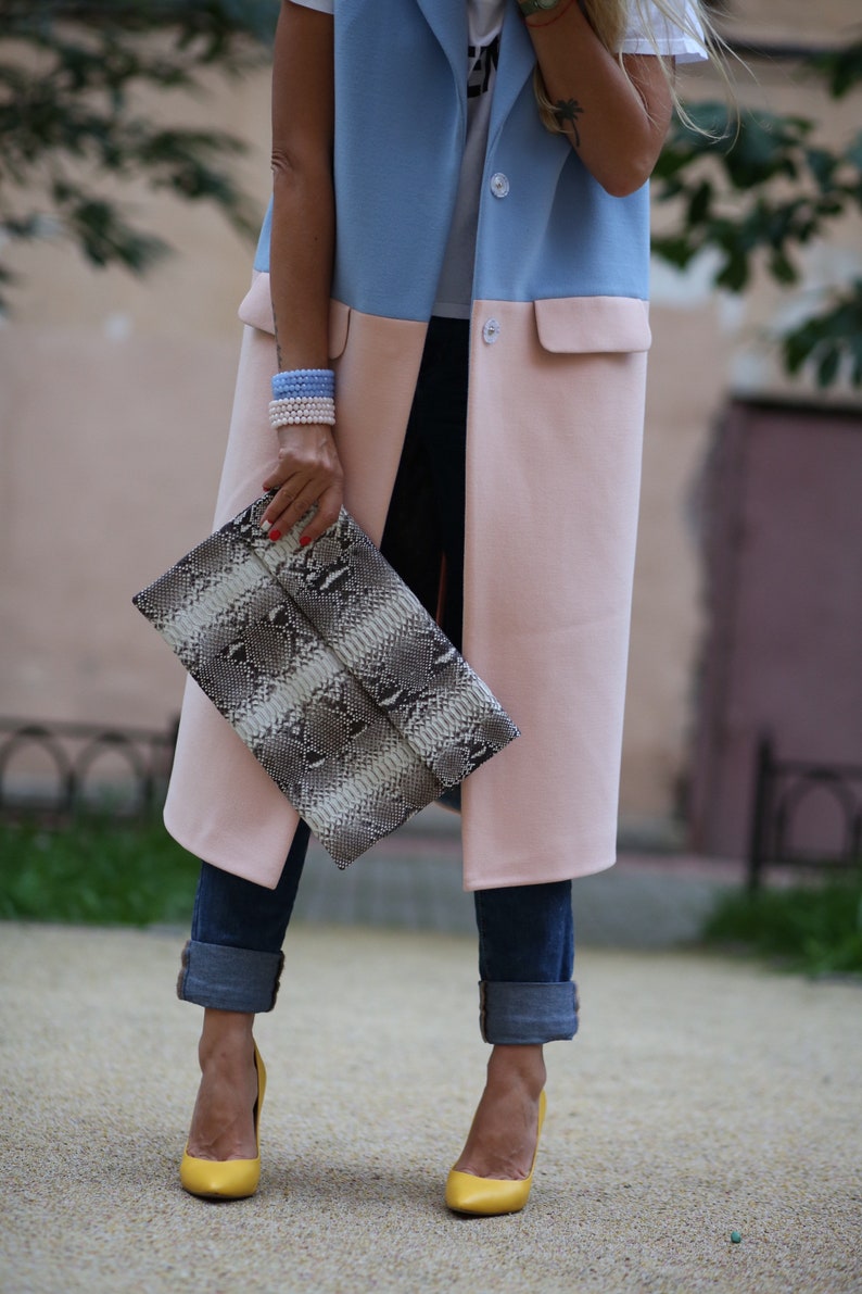 May include: A woman wearing a blue and pink long vest with a snakeskin clutch and yellow heels.