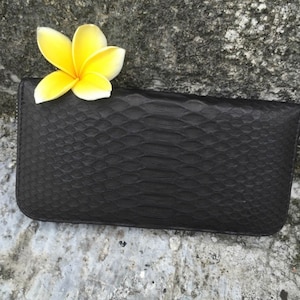 May include: A black leather wallet with a snakeskin pattern. A yellow flower is on top of the wallet.