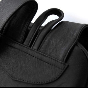 以下が含まれることがあります： 調節可能なストラップが付いた黒い革のバックパックのクローズアップ。ストラップは厚手の革製で、滑らかな仕上がりです。