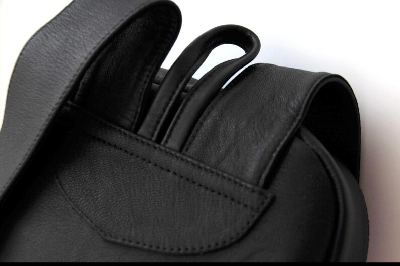 以下が含まれることがあります： 調節可能なストラップが付いた黒い革のバックパックのクローズアップ。ストラップは厚手の革製で、滑らかな仕上がりです。