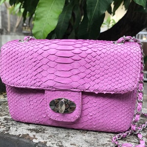 K&ouml;nnte beinhalten: Eine kleine, lavendelfarbene Handtasche aus Schlangenleder mit einer silbernen Kettenkette und einem silbernen Verschluss.