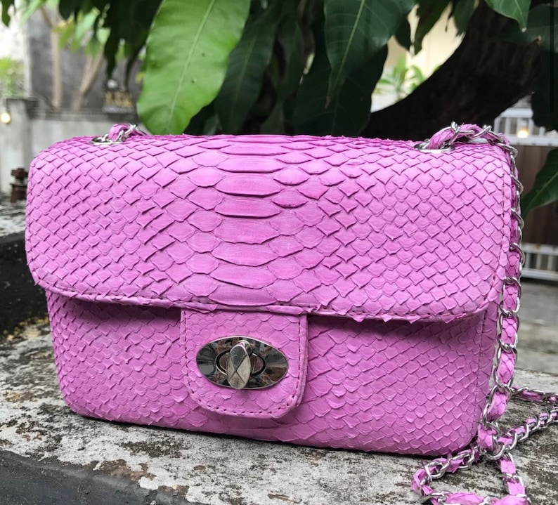 K&ouml;nnte beinhalten: Eine kleine, lavendelfarbene Handtasche aus Schlangenleder mit einer silbernen Kettenkette und einem silbernen Verschluss.