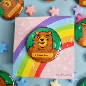 Pode incluir: Um urso pixelado verde e marrom com o texto "I choose bear." em um fundo verde. O urso está em um botão redondo com um fundo de arco-íris e o texto "pastelheeks" no canto inferior direito.