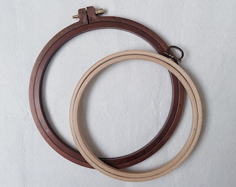 May include: Two embroidery hoops, one brown and one natural wood, are nested together. The brown hoop has a metal screw closure.