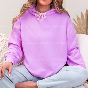 May include: A light purple hoodie with a drawstring hood. The hoodie is a solid color and has long sleeves. The text "RHODY ORIGINALS" is visible on the hoodie. The person is wearing light blue jeans.