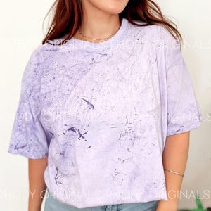 Pode incluir: Uma camiseta tie-dye de cor lil&aacute;s claro com um caimento relaxado. A camiseta tem um visual desbotado e vintage com um padr&atilde;o sutil de m&aacute;rmore.