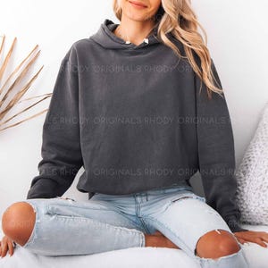 May include: A dark gray hoodie with a drawstring hood and long sleeves. The hoodie is worn with light blue ripped jeans. The text "RHODY ORIGINALS" is visible on the hoodie. The overall theme is casual wear.