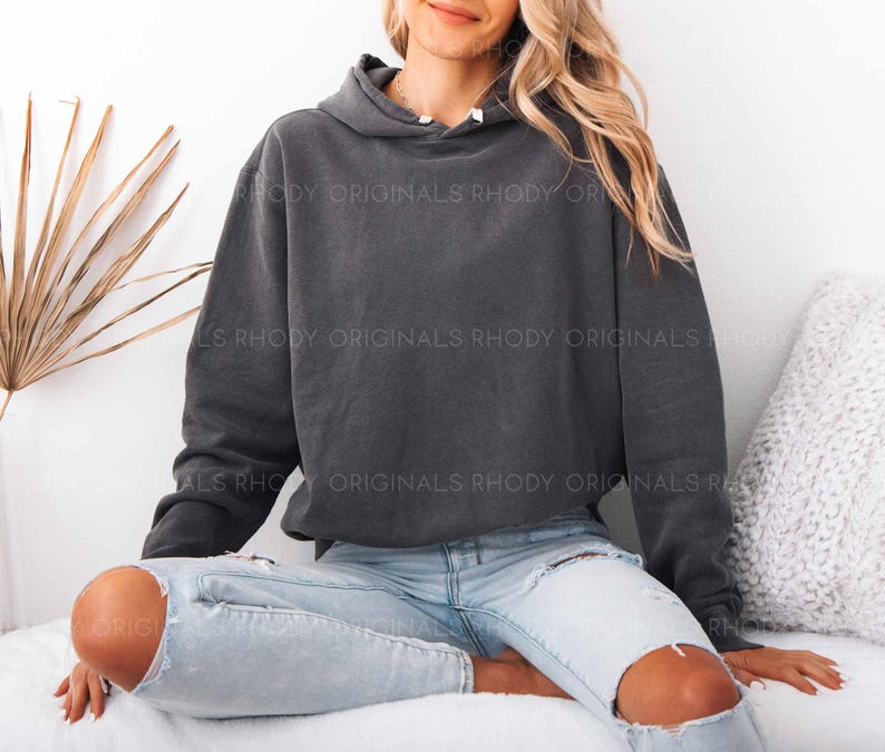 May include: A dark gray hoodie with a drawstring hood and long sleeves. The hoodie is worn with light blue ripped jeans. The text "RHODY ORIGINALS" is visible on the hoodie. The overall theme is casual wear.