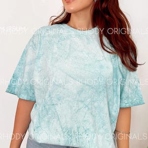 Pode incluir: Uma camiseta azul claro tie-dye com um caimento relaxado. A camiseta tem um visual desbotado e vintage.