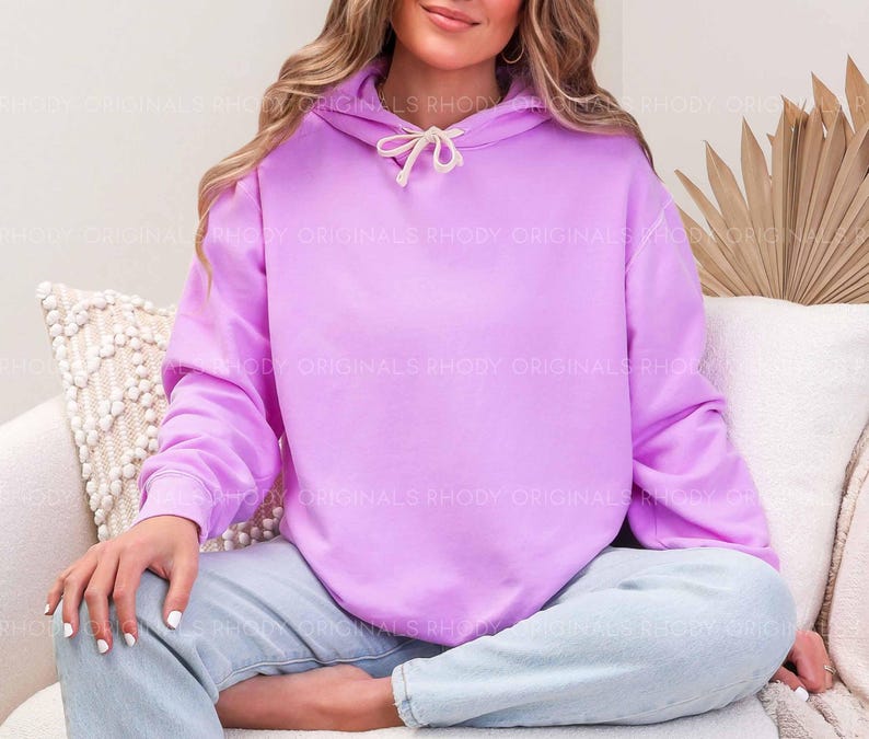 May include: A light purple hoodie with a drawstring hood. The hoodie is a solid color and has long sleeves. The text "RHODY ORIGINALS" is visible on the hoodie. The person is wearing light blue jeans.
