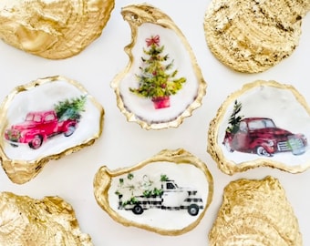 May include: Decorative oyster shells with gold edges. Some shells feature Christmas-themed images, including a red truck carrying a Christmas tree, a Christmas tree in a pot, and a black and white truck with flowers.