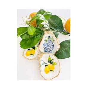 May include: Three oyster shell dishes with gold trim. One dish features a blue and white porcelain design, while the other two feature yellow lemons with green leaves.