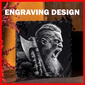 May include: A black slate coaster featuring a detailed grayscale engraving of a Viking warrior with an axe. The text "ENGRAVING DESIGN" is in white at the top. The coaster has a rough, natural edge, and is likely 10 cm x 10 cm.