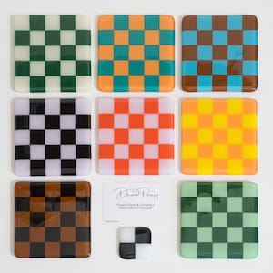 May include: Nine square ceramic coasters with a checkerboard pattern in various colours, including black, white, green, orange, red, yellow, brown, and blue. The coasters are handcrafted in Cornwall by David Perry.