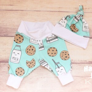 May include: A baby outfit set with a light blue and white milk carton and cookie print. The set includes a pair of pants and a hat. The hat has a knot on top. The pants have a white elastic waistband and white cuffs. The text "Hartley Jax Kids" is printed on the bottom right corner of the image.