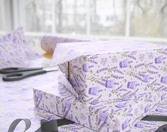 May include: Wrapping paper featuring a repeating pattern of light purple boba tea cups, lavender sprigs, small butterflies, and tiny mushrooms on a white background. The paper is shown covering rectangular boxes with black scissors nearby.