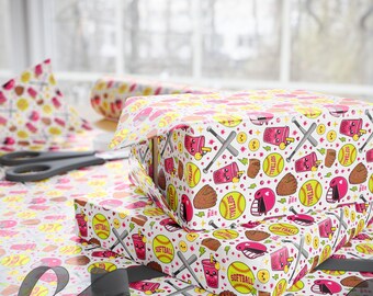 May include: White wrapping paper featuring a repeating pattern of yellow softballs, brown baseball gloves, grey bats, pink helmets, and pink boba tea cups with faces. The design includes small green lightning bolts and hearts throughout the print.