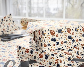 May include: Wrapping paper featuring a repeating pattern of brown footballs, dark blue helmets, yellow goalposts, and dark blue buckets on a cream background. The paper is shown covering two rectangular boxes, with a roll and scissors nearby.