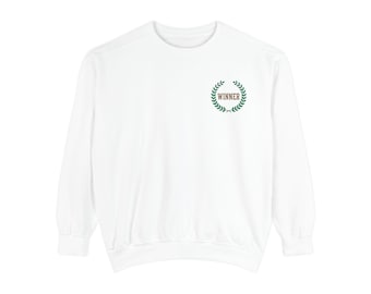 May include: A white long-sleeve sweatshirt featuring a small embroidered design on the upper left chest. The design consists of a green laurel wreath encircling the word WINNER printed in a brown, capitalized, serif font.