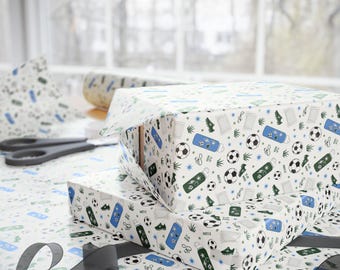 May include: White wrapping paper featuring a repeating pattern of soccer balls, green cleats, soccer goals, and blue or green water bottles with the text PLAY HARD. The paper is wrapped around rectangular boxes with black scissors nearby.
