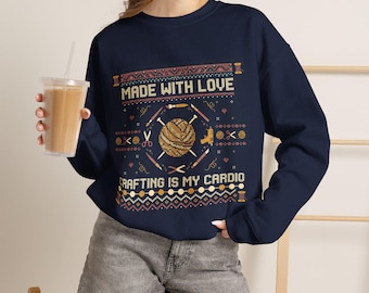 May include: A navy blue crewneck sweatshirt featuring a graphic print with the text "MADE WITH LOVE" and "CRAFTING IS MY CARDIO". The design includes illustrations of a yarn ball, knitting needles, scissors, and a glue gun.