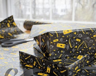 May include: Wrapping paper featuring a repeating pattern of yellow athletic shoes, lightning bolts, batteries, stopwatches, and trophies on a black background. The paper is shown covering two rectangular boxes, with a black ribbon visible in the foreground.