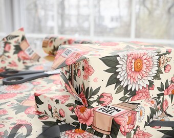 May include: Gift-wrapped boxes and wrapping paper featuring a floral design with pink and white flowers, green leaves, and the text "MOM FUEL". The wrapping paper is beige with a repeating floral pattern. A pair of scissors and a roll of paper are also visible.