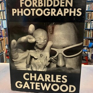 May include: A book titled "Forbidden Photographs" by Charles Gatewood. The cover features a black and white image of a person wearing sunglasses and a small figure. The title and author's name are in white text.