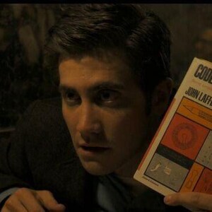 May include: A man is looking intently at a book titled "Codes and Ciphers" by John Laffin. The book cover features a yellow background with orange and red squares containing various symbols and diagrams.