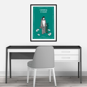 May include: A framed poster with a green background featuring a cartoon illustration of a person in a gray costume holding an axe. The text "DONNIE DARKO" is at the top of the poster.