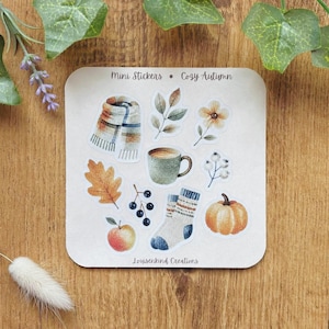 Könnte beinhalten: Ein Stickerbogen mit dem Titel Mini Stickers - Cozy Autumn von Louisenkind Creations mit Aquarellillustrationen eines karierten Schals, Herbstblättern, einer Blume, einer grünen Tasse, Beeren, einer Socke, einem Apfel und einem orangefarbenen Kürbis.
