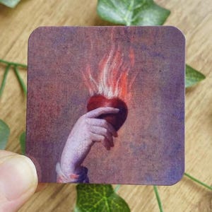 Könnte beinhalten: Ein quadratischer Aufkleber mit einer Hand, die ein brennendes Herz hält. Das Kunstwerk hat eine Vintage-Ästhetik mit einer Farbpalette aus Rot, Lila und Braun. Der Aufkleber dient wahrscheinlich dekorativen Zwecken.