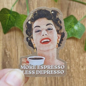 Könnte beinhalten: Ein gestanzter Aufkleber mit einer Illustration im Vintage-Stil einer Person mit dunklem Haar, goldenen Ohrringen und rotem Lippenstift, die eine weiße Kaffeetasse hält. Der Text am unteren Rand lautet MORE ESPRESSO LESS DEPRESSO in fetten weißen Großbuchstaben.